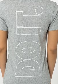 Camiseta de algodón gris con grandes letras blancas en bloque que dicen "hazlo" y un círculo, con una textura suave y ligera y un corte clásico.