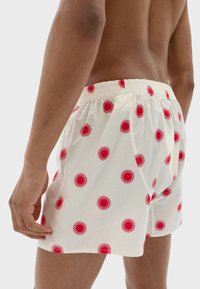 Miesten boxerit, joissa on kerma kangas ja punaisia pyöreitä kuvioita. Niissä on kuminauhavyötärö ja löysä istuvuus. Rakenteellinen puuvillamateriaali.