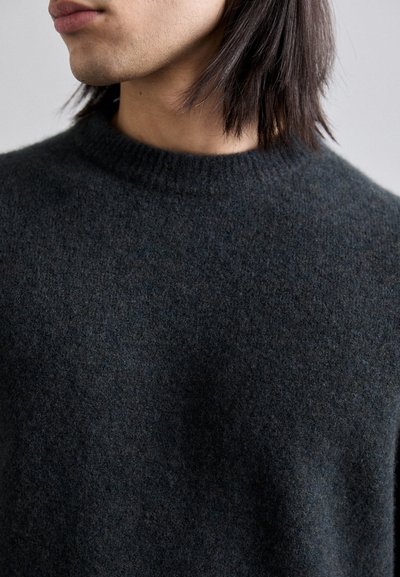 Pull en laine gris foncé avec un col rond, composé d'un tissu doux et légèrement texturé, et d'une coupe décontractée. La bordure du col est côtelée.