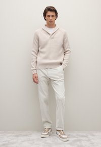 Beiger gerippter Strickpullover mit Schalkragen, kombiniert mit hellbeigen Cordhosen und weißen Sneakern mit beigen Akzenten.