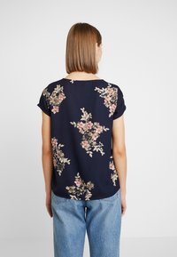 Námořnická květinová halenka s krátkým rukávem, s růžovými a krémovými květinami, kulatým výstřihem, měkkou tkaninou, volným střih a mírně zakřiveným spodním lemem.