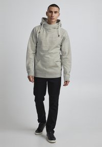 Sweatshirt à capuche gris clair avec un motif texturé, poche avant et cordons de serrage. Assorti avec un jean noir et des baskets noires.