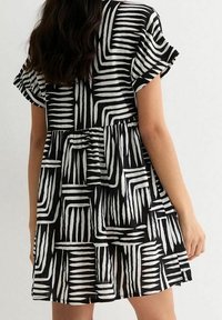 Zwart-witte jurk met korte mouwen, met geometrische strepen. Valt soepel vanaf de taille met een rimpelrand.