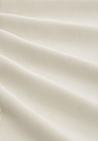 Krämfärgad tyg med en slät, matt textur draperad i mjuka veck, som visar subtila linjer och ett enhetligt mönster.