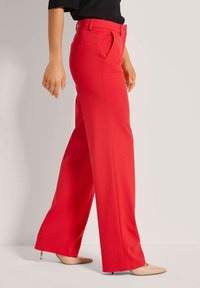 Rote maßgeschneiderte Hosen mit hoher Taille, geradem Schnitt und Seitentaschen, kombiniert mit nacktfarbenen Absätzen. Glatte Textur und präzise Verarbeitung.