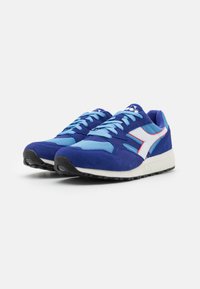 Blue athletic shoes featuring a mix of suede and mesh materials, white logo, contrasting light blue accents, and black rubber outsole.