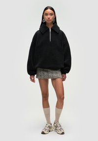 Czarny polarowy pulower z kołnierzem i półzamkiem, zestawiony z mini spódniczką w wzór houndstooth. Modelka nosi skarpety do kolan i trampki.