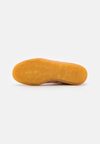 Sole tenisky s texturovanou gumovou podrážkou jasně oranžové barvy s kulatými vzory; bok je pokryt růžovým a šedým vrchním materiálem.