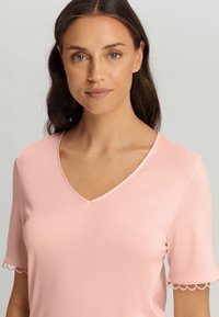 Maglietta rosa a maniche corte con scollatura a V e orlo smerlato sulle maniche, realizzata in un tessuto morbido con una superficie liscia, ideale per un look casual.