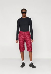 Zwarte top met lange mouwen gecombineerd met hooggetailleerde, bordeauxrode gewatteerde shorts met een gladde structuur en zichtbare stikseldetails. Zwarte sneakers.