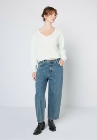 Licht muntgroene cropped sweater met V-hals, gecombineerd met losse blauwe jeans en zwarte enkellaarsjes. Soepele textuur met casual ontwerp.