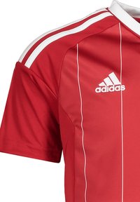 Maglia atletica rossa a maniche corte, con strisce bianche lungo le spalle e un piccolo logo Adidas sul petto. Texture liscia.