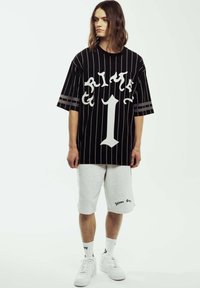 Camisa oversize a rayas negras con gráfico blanco "GRIME" y el número uno; combinada con pantalones cortos grises y zapatillas blancas.