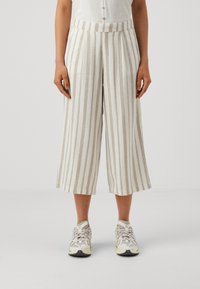 Linneblandning culotter har vertikala beige och vita ränder, en vida passform och ett högt midjeband, parat med ljusa atletiska sneakers.