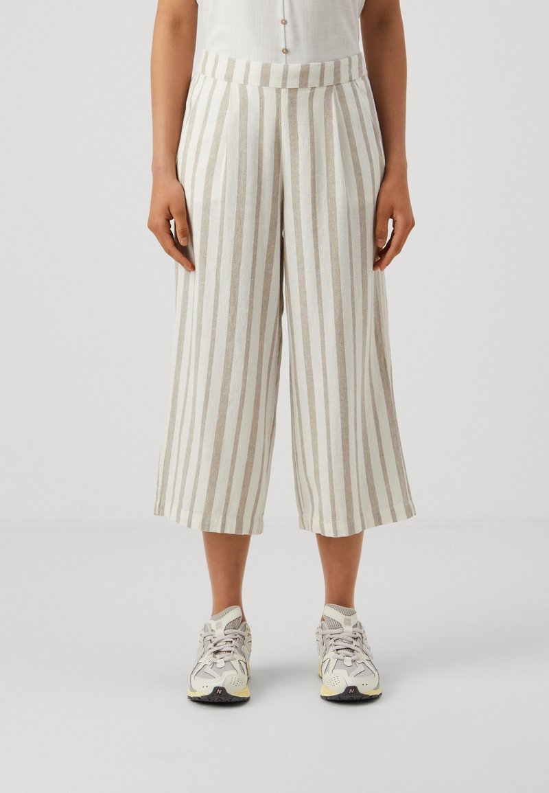 Linneblandning culotter har vertikala beige och vita ränder, en vida passform och ett högt midjeband, parat med ljusa atletiska sneakers.