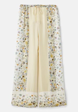 Spodnie o szerokich nogawkach w kwiatowy wzór mają jasny żółty kolor z białymi kwiatowymi wzorami w fioletowych, pomarańczowych i zielonych akcentach. Regulowany pas.