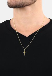 Man med ett guldkedjehalsband med ett litet tvåfärgat kors hängande över en svart V-ringad tröja.