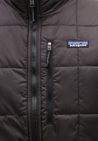 Μαύρο καπιτονέ μπουφάν Patagonia με κεντρικό φερμουάρ και φερμουάρ σε τσέπη στο στήθος που φέρει το λογότυπο της μάρκας.