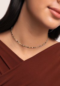 Collier ras du cou en perles avec de petites perles colorées dans des teintes de rose, vert et noir, avec des accents dorés, reposant sur un décolleté.