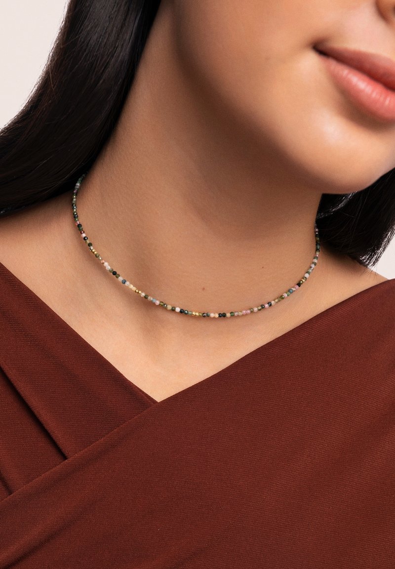 Collier ras du cou en perles avec de petites perles colorées dans des teintes de rose, vert et noir, avec des accents dorés, reposant sur un décolleté.