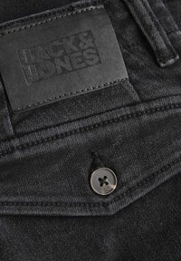 Svarta jeans i denim med en strukturerad tyg, synliga sömmar, en metallknapp och en rektangulär läderlapp med "JACK & JONES" präglat.