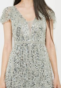 Glitzerndes, durchsichtiges Kleid mit tiefem V-Ausschnitt, kurzen Puffärmeln, aufwendigem Paillettenmuster in Silber und schillernden Tönen sowie geschichteter Textur.