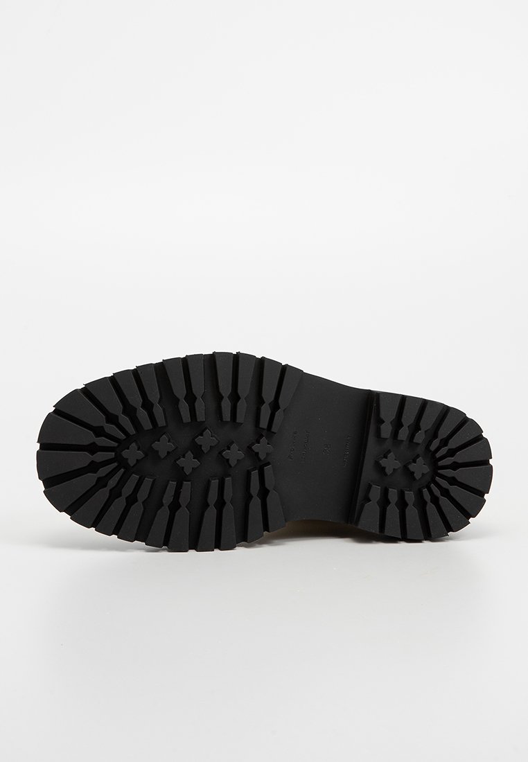 Czarna, gumowa podeszwa buta z teksturowanym, bieżnikowanym wzorem dla lepszej przyczepności. Posiada wypukłe sekcje oraz gładką centralną część.