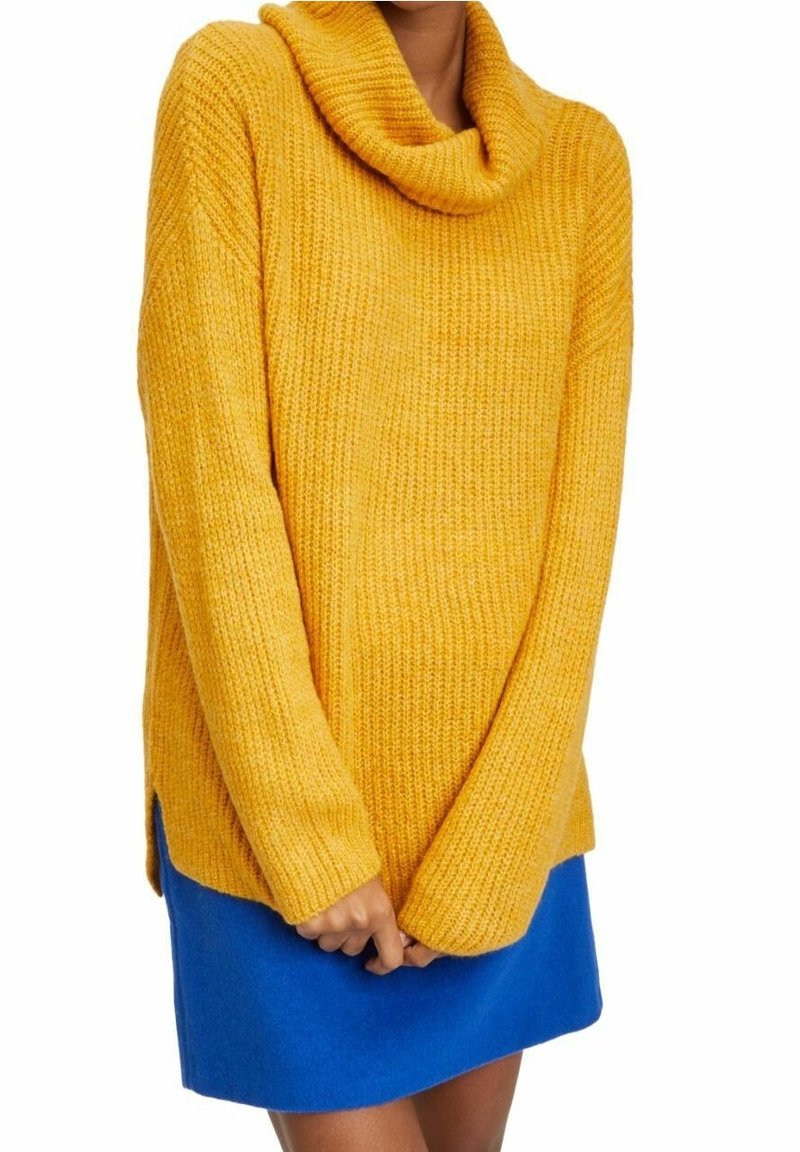 Gul stickad tröja med ringkrage och långa ärmar, kombinerad med en blå kjol. Texturen är ribbad och passformen är lös.