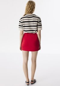 Pull en laine rayé noir et cr�ème, associé à une mini-jupe rouge ajustée. Détails comprenant un col et une ceinture élastique.