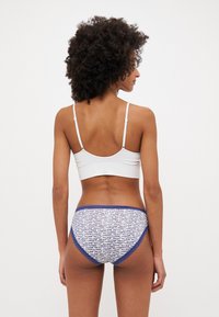 Valge ribadega bralette, mille juurde kuuluvad siniste mustritega aluspesu, millel on tekstuuriga vöökoht ja kontrastne sinine äär. Vaade tagant.