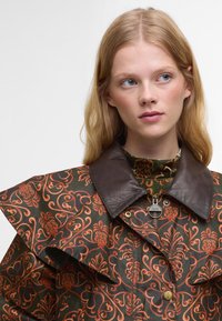 Gestepptes Jacket mit orangefarbenen Blumenmustern auf einem dunkelgrünen Hintergrund, versehen mit einem braunen Lederkragen und metallischen Reißverschlussdetails.