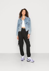 Traper jakna svijetloplave boje s oštećenim rubom, bijeli cropped top, crne cargo hlače s bočnim džepovima i ljubičaste Nike tenisice.