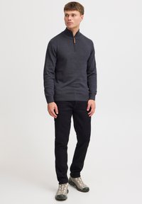 Haut à col zippé mi-long gris foncé en tricot texturé, associé à un pantalon noir et des baskets grises avec une semelle épaisse et des accents clairs.