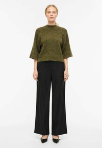 Maglione verde di lana a maniche corte, abbinato a pantaloni neri a gamba larga e scarpe nere con tacco. Design semplice e tessuto texturizzato.