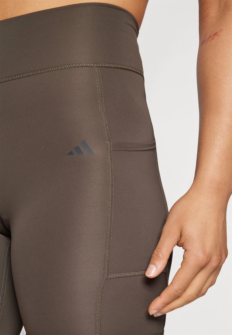 Leggings deportivas marrones con una cintura alta, detalles de costura sutiles y un bolsillo lateral con un acento de logo negro.