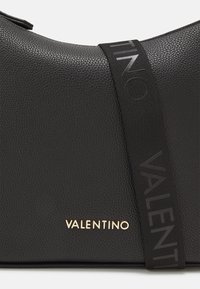 Borsa a mano in pelle nera con superficie texturizzata, logo dorato "VALENTINO" e tracolla nera con lettering in rilievo.