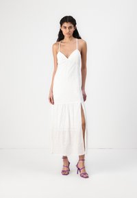 Rochie maxi albă cu bretele subțiri, decolteu în formă de V, material texturat și o fanta pe lateral. Asortată cu sandale cu toc înalt mov.