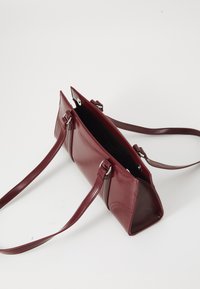 Borsa a mano in pelle borgogna con forma rettangolare, due tracolle regolabili e hardware in argento. La parte superiore aperta rivela un interno foderato.