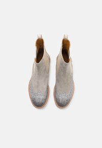 Stivaletti alla caviglia in suede grigio chiaro con punta in metallo argentato e dettagli perforati. Fodera e cuciture in pelle marrone, linguette laterali per una facile calzata.