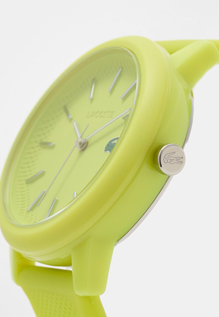 Żółty zegarek na rękę Lacoste z srebrnymi znacznikami godzin, białymi wskazówkami oraz logo krokodyla na tarczy i koronie, widok pod kątem.