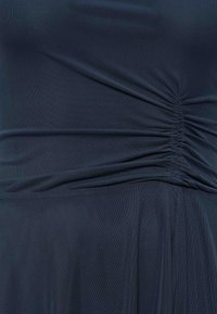 Tissu bleu foncé avec un détail froncé qui crée des plis horizontaux et de la texture sur un matériau lisse.