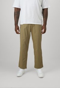 Beige, locker sitzende Hosen mit geradem Schnitt. Getragen mit einem weißen T-Shirt und weißen Sneakers. Glatte Textur, keine sichtbaren Muster.