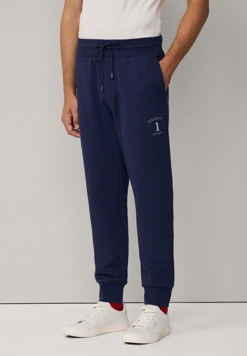 Marine joggers met elastische tailleband en aantrekkoord, voorzien van zijzakken en een geprinte logo op de linker bovenbeen. Gemaakt in combinatie met witte sneakers.