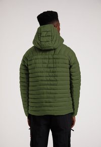 Olivgrön pufferjacka med horisontellt quiltat mönster, fastsydd huva och texturerat tyg. Bärs med svarta cargobyxor, vilket ger en sportig look.