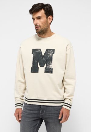 Cream-colored sweatshirt featuring a large distressed gray "M" logo on the front, with striped cuffs and hem. Material appears soft and textured.