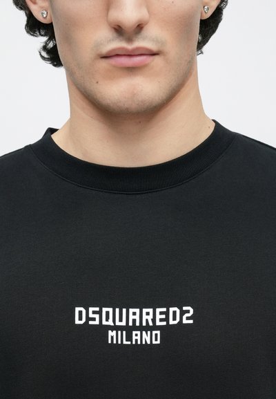 Melna kokvilnas T-krekls ar apaļu kakla izgriezumu, centrā baltā krāsā uzdrukāts teksts "DSQUARED2 MILANO". Gluda tekstūra ar ribotu apkakli.