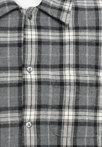 Harmaa ruudullinen flanellipaita, jossa mustavalkoinen ruutukuosi, napitettava edessä ja perinteinen kaulus, pehmeästä materiaalista.