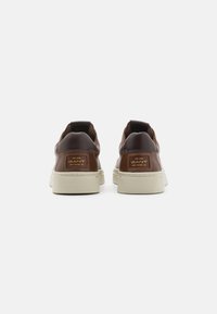 Ein Paar braune Leder-Sneaker mit weißen Sohlen, die die Rückansicht zeigen, mit "GANT New Haven, CT"-Labels auf jeder Ferse.