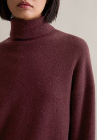 Burgundowa sweter z golfem w miękkim, teksturowanym splocie o dopasowanym kroju. Prosty design z prążkowanym kołnierzem i luźnymi ramionami.