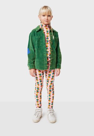Chaqueta de pana verde con acento azul, leggings rosas con estampado de cajas de regalo coloridas y zapatillas blancas.